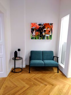 Hörgeräte Reichart Schwabing-West – gemütlicher Warteraum mit stilvollem Sofa und Kunst für einen angenehmen Aufenthalt.