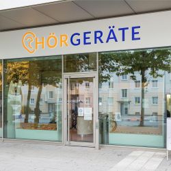 Außenansicht der Filiale München Pasing: Hörgeräte Reichart Geschäft mit großer Fensterfront, einladend und modern gestaltet.